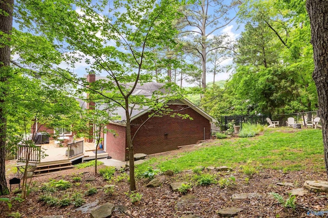 view of property exterior featuring brick siding, fence, a chimney, and a deck