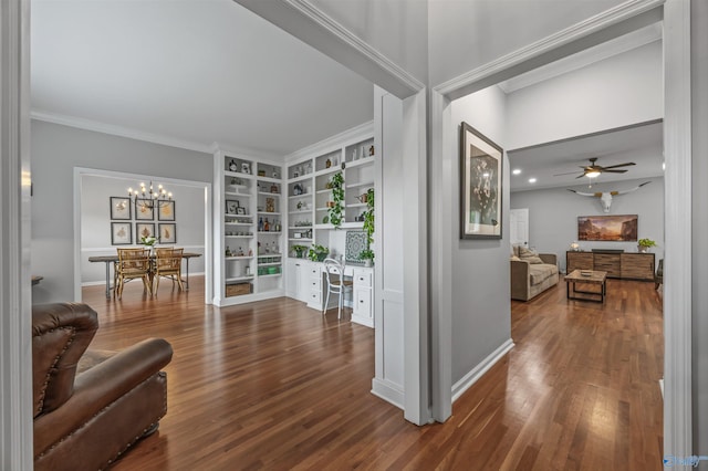living area with crown molding, built in study area, built in shelves, ceiling fan with notable chandelier, and wood finished floors