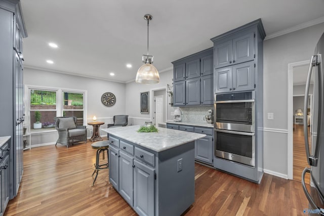 kitchen featuring gray cabinets, a kitchen island, dark wood finished floors, ornamental molding, and stainless steel appliances