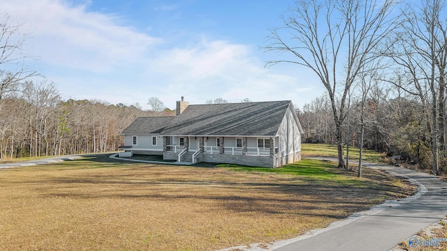 view of front of property featuring a front yard, a forest view, a chimney, and covered porch