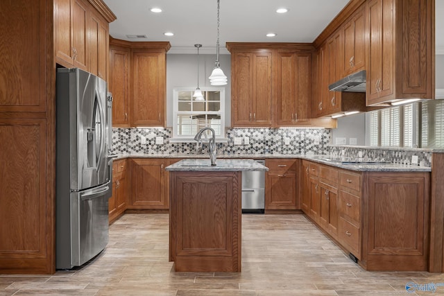 kitchen featuring under cabinet range hood, a kitchen island with sink, brown cabinets, and appliances with stainless steel finishes