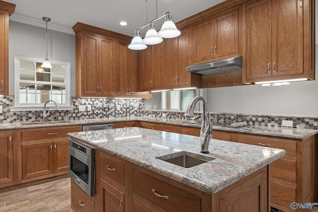 kitchen featuring brown cabinetry, under cabinet range hood, a sink, and appliances with stainless steel finishes