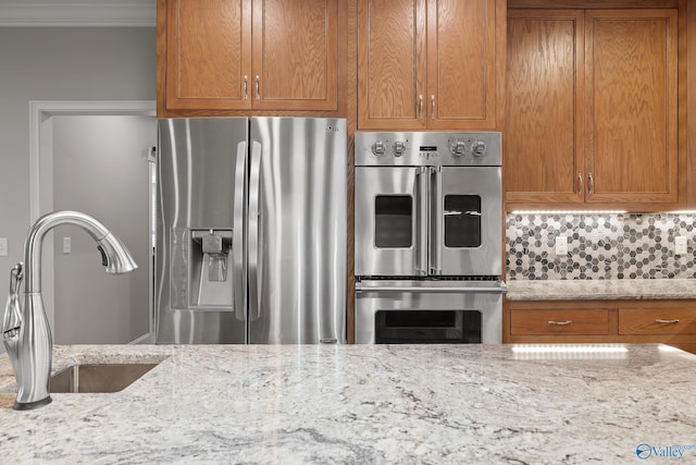 kitchen with ornamental molding, light stone counters, brown cabinetry, appliances with stainless steel finishes, and a sink
