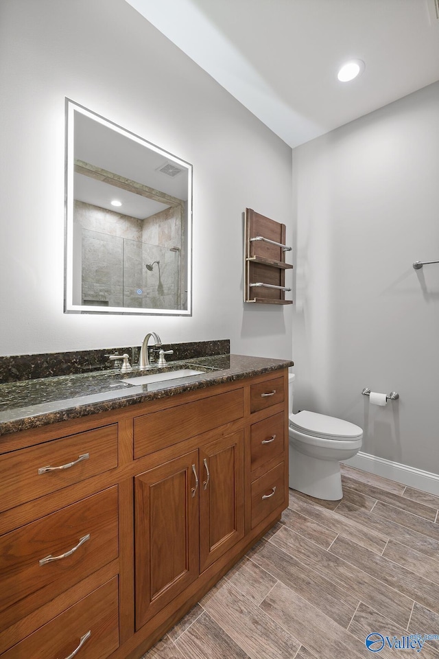 bathroom featuring a tile shower, wood finish floors, vanity, toilet, and baseboards