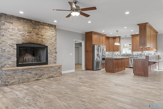 kitchen featuring appliances with stainless steel finishes, a ceiling fan, light wood-style flooring, a kitchen island, and decorative backsplash