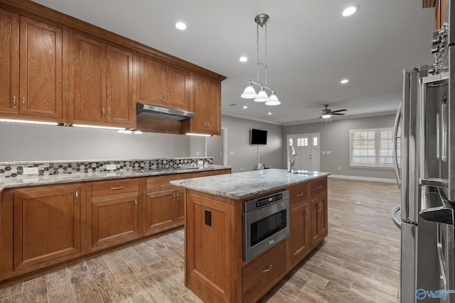 kitchen with under cabinet range hood, freestanding refrigerator, brown cabinetry, and a ceiling fan