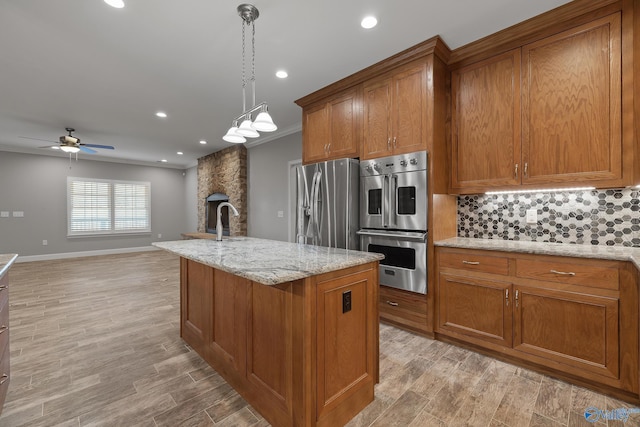 kitchen featuring tasteful backsplash, appliances with stainless steel finishes, a ceiling fan, light wood-style floors, and brown cabinets