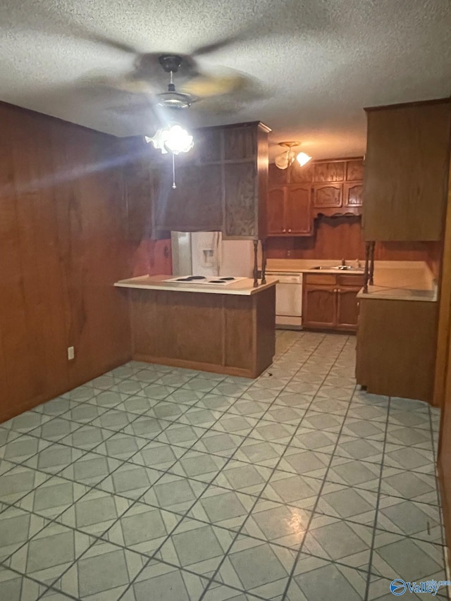 kitchen with brown cabinets, a ceiling fan, a sink, wooden walls, and a peninsula