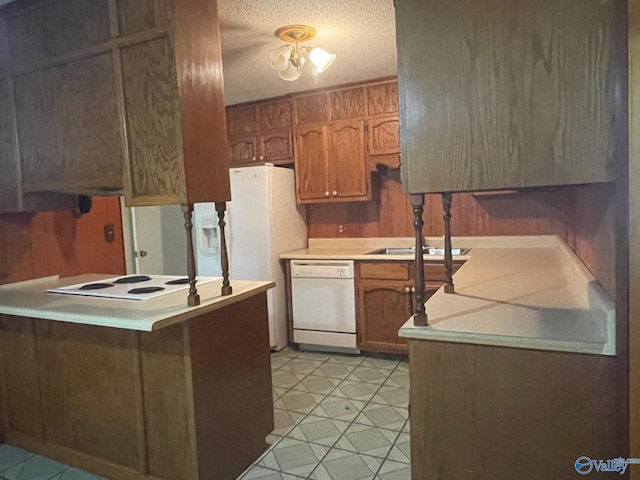 kitchen with a peninsula, white dishwasher, cooktop, light countertops, and a textured ceiling