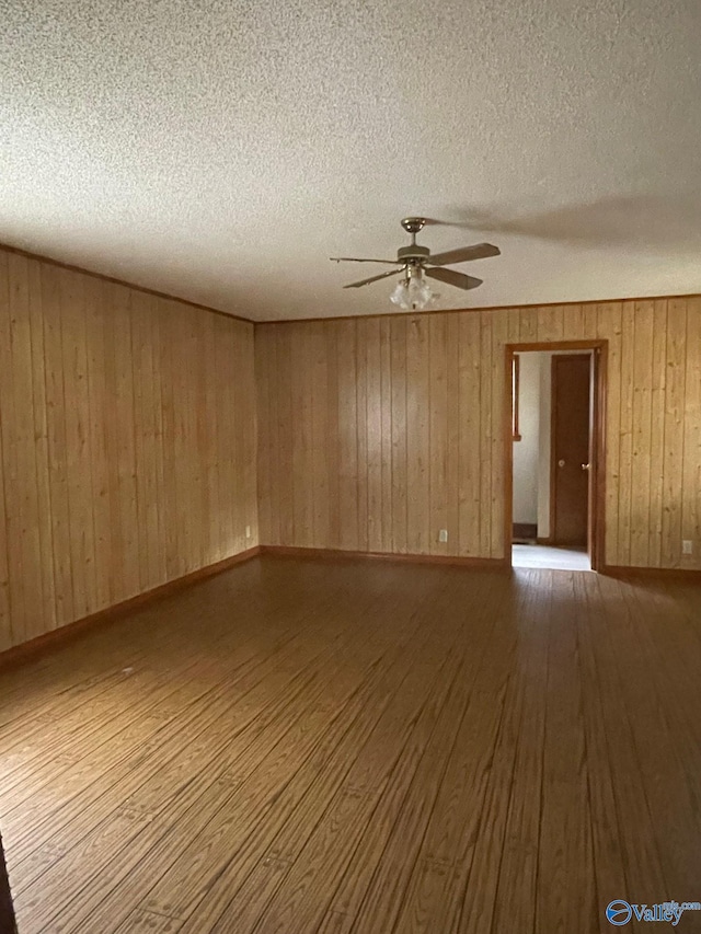 unfurnished room with a ceiling fan, wood finished floors, baseboards, wood walls, and a textured ceiling