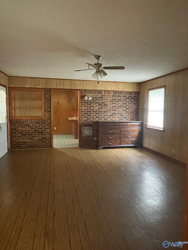 unfurnished living room with ceiling fan, wooden walls, hardwood / wood-style floors, and a textured ceiling