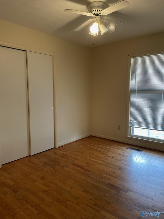 unfurnished bedroom with a closet, visible vents, a ceiling fan, and wood finished floors