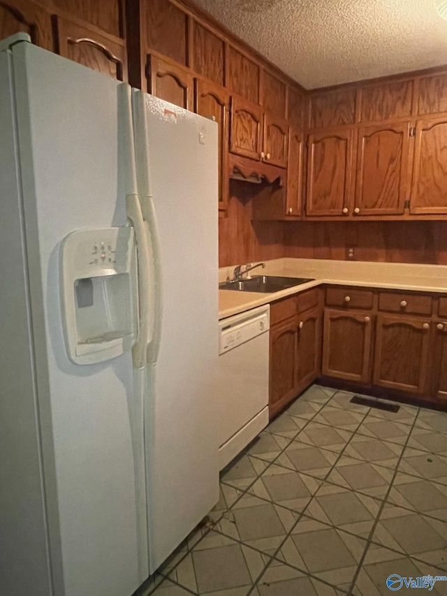 kitchen featuring white appliances, a sink, light countertops, a textured ceiling, and brown cabinets