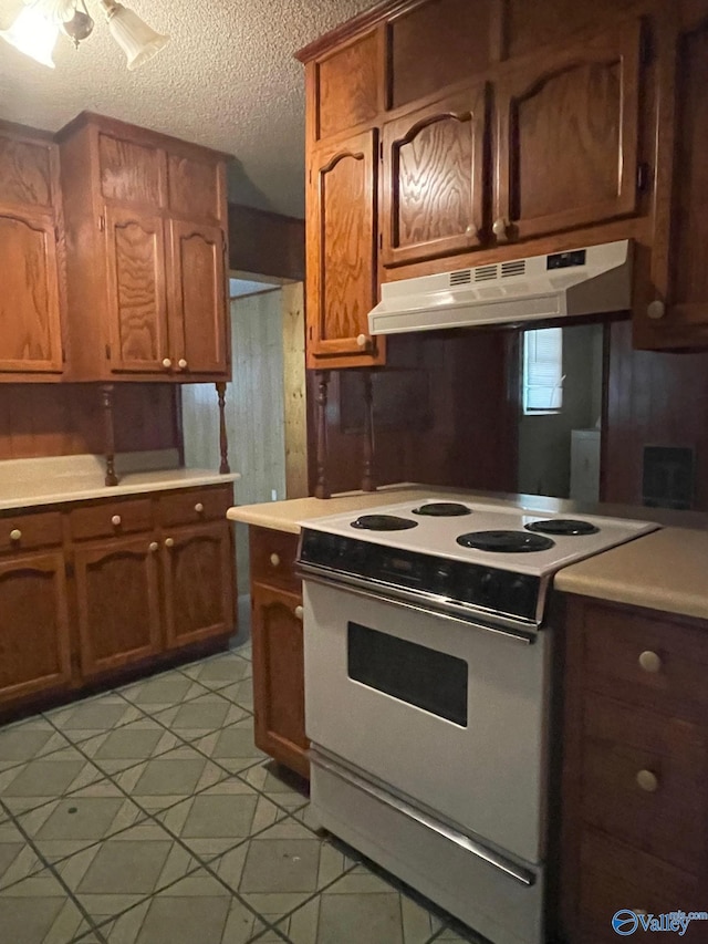 kitchen with white range with electric cooktop, under cabinet range hood, light countertops, brown cabinetry, and a textured ceiling