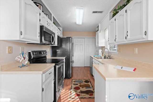 kitchen with white cabinets, sink, light hardwood / wood-style flooring, a textured ceiling, and stainless steel appliances