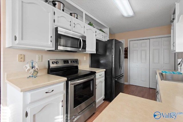 kitchen featuring appliances with stainless steel finishes, a textured ceiling, sink, dark hardwood / wood-style floors, and white cabinetry