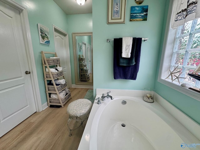 bathroom with a garden tub, wood finished floors, and baseboards