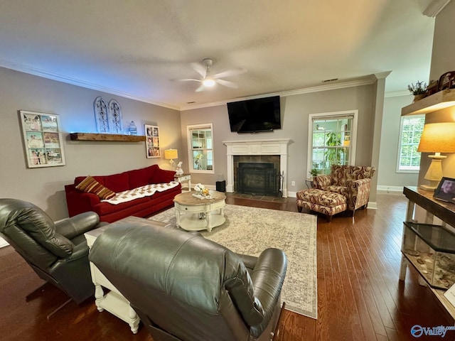 living area featuring a ceiling fan, a tile fireplace, baseboards, ornamental molding, and dark wood-type flooring