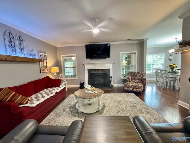 living area with a ceiling fan, wood finished floors, a tiled fireplace, baseboards, and ornamental molding