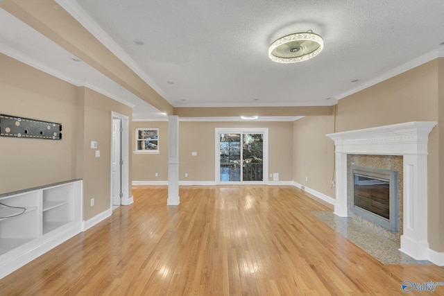 unfurnished living room featuring a high end fireplace, light wood-type flooring, decorative columns, ornamental molding, and a textured ceiling