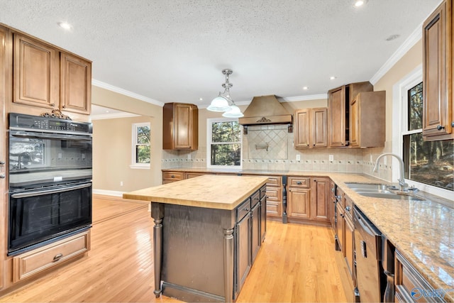 kitchen with ornamental molding, a textured ceiling, black double oven, light hardwood / wood-style flooring, and a kitchen island