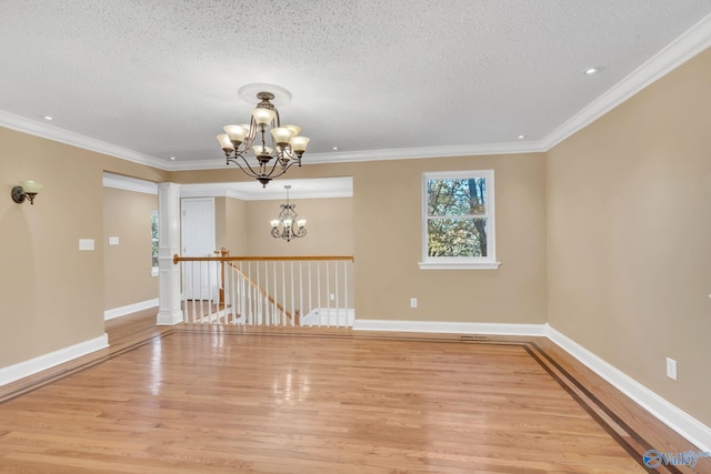 empty room featuring ornamental molding, light hardwood / wood-style floors, a textured ceiling, and an inviting chandelier