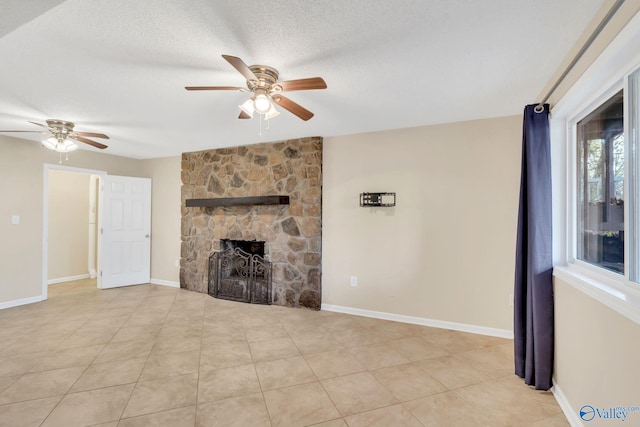 unfurnished living room with a textured ceiling, ceiling fan, light tile patterned floors, and a stone fireplace