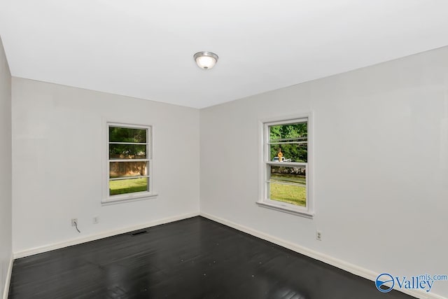 empty room with dark wood finished floors, baseboards, and visible vents