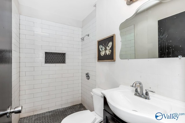 bathroom featuring tasteful backsplash, tile walls, toilet, tiled shower, and vanity