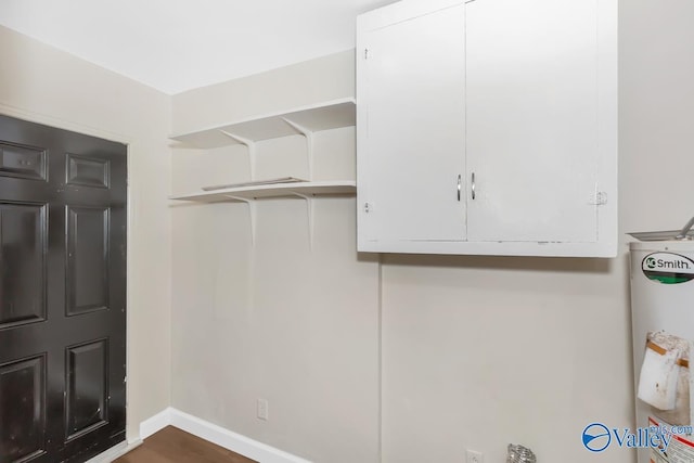 clothes washing area with water heater, baseboards, and wood finished floors