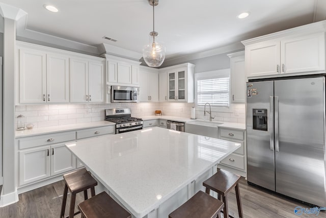 kitchen featuring sink, stainless steel appliances, pendant lighting, a kitchen bar, and white cabinets