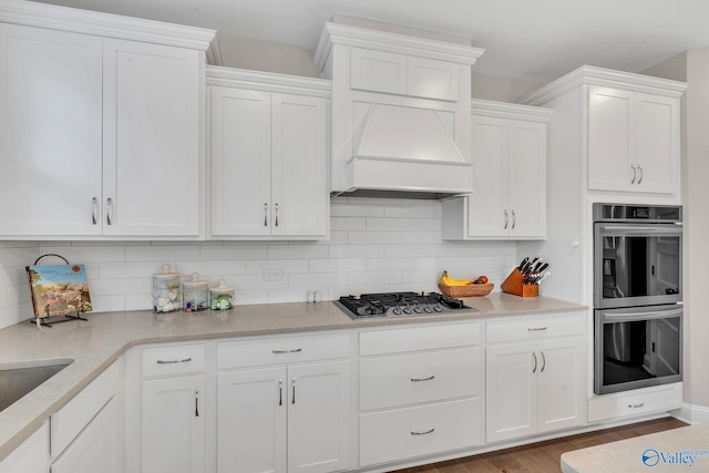 kitchen featuring appliances with stainless steel finishes, white cabinetry, decorative backsplash, custom range hood, and light hardwood / wood-style flooring