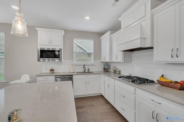 kitchen featuring pendant lighting, white cabinetry, sink, stainless steel appliances, and custom range hood