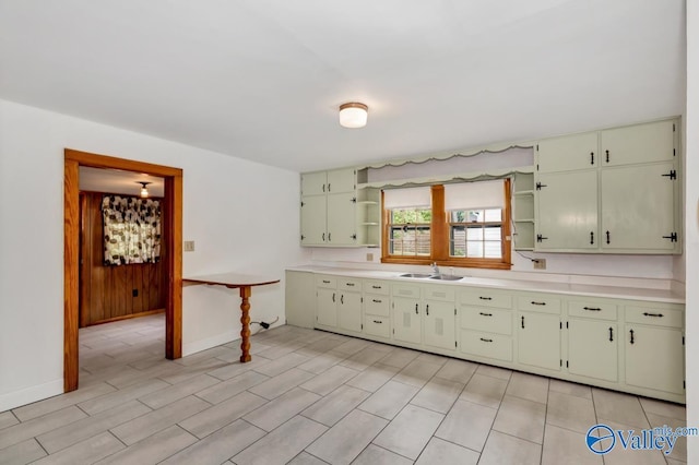 kitchen with open shelves, baseboards, light countertops, and a sink