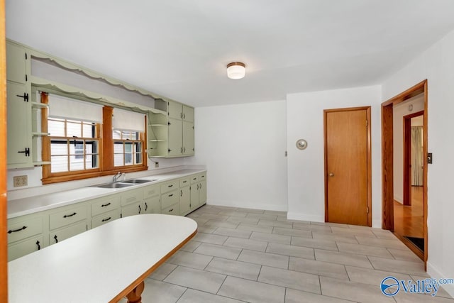 kitchen featuring open shelves, light countertops, green cabinets, and a sink