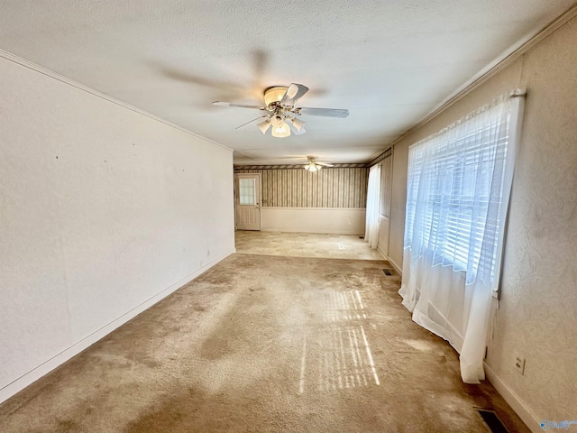 empty room featuring light carpet, ceiling fan, crown molding, and a textured ceiling