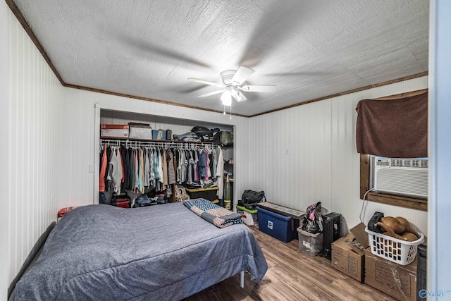 bedroom featuring wood-type flooring, cooling unit, ornamental molding, a textured ceiling, and a closet