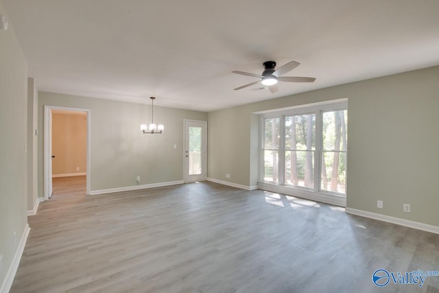 empty room featuring light hardwood / wood-style floors, a wealth of natural light, and ceiling fan with notable chandelier