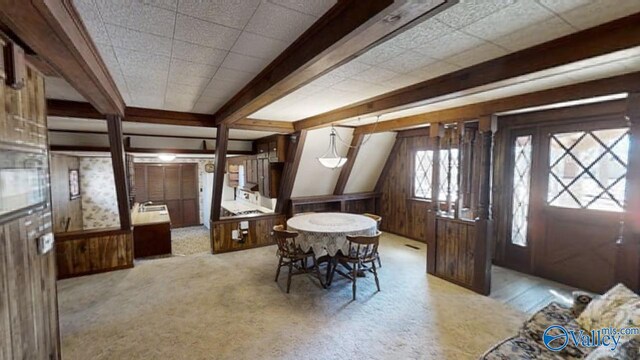 carpeted dining area with beamed ceiling and wood walls