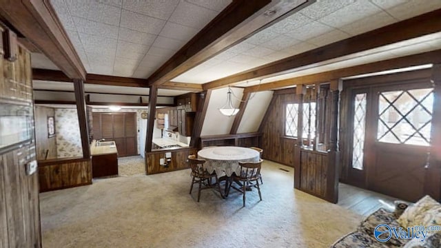 carpeted dining room featuring beam ceiling and wood walls