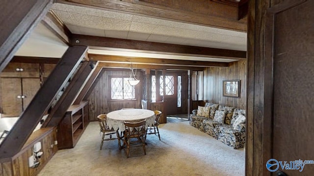 dining room with light carpet, beamed ceiling, and wood walls