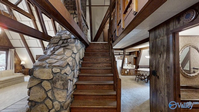 stairs with beamed ceiling, wooden walls, and carpet floors