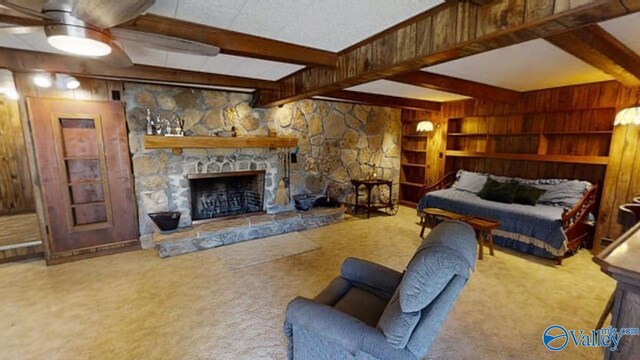 living room with beamed ceiling, wooden walls, a fireplace, carpet, and ceiling fan