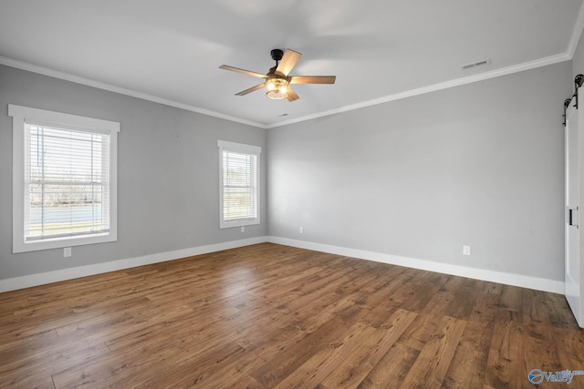 empty room featuring wood finished floors, crown molding, baseboards, and a barn door