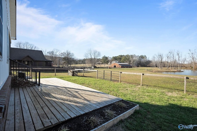 view of yard with fence, a deck with water view, and a rural view