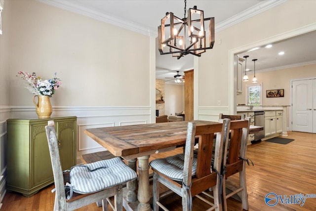 dining area featuring light wood-style flooring, crown molding, a wainscoted wall, and ceiling fan with notable chandelier