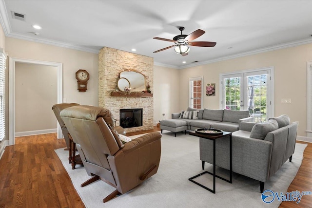 living area with a ceiling fan, light wood finished floors, a fireplace, ornamental molding, and visible vents