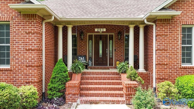 view of exterior entry featuring brick siding, roof with shingles, and covered porch