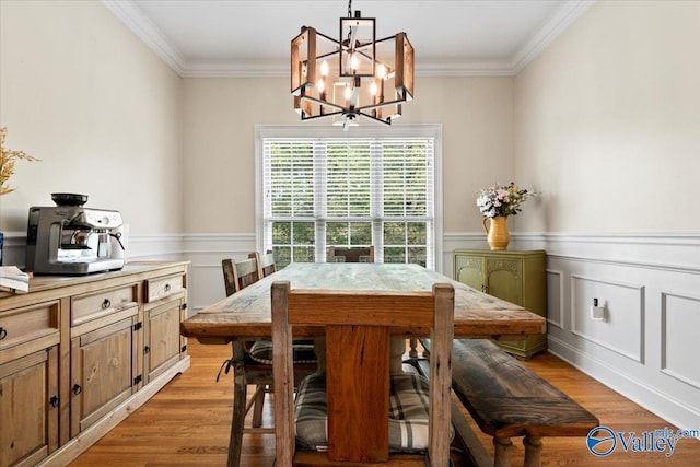 dining room featuring a chandelier, light wood-style floors, crown molding, and a wainscoted wall