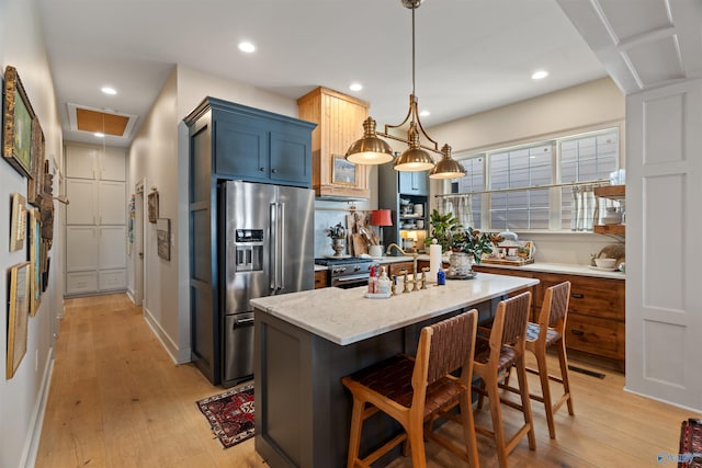 kitchen with light stone counters, pendant lighting, a kitchen island, stainless steel fridge with ice dispenser, and light wood-type flooring